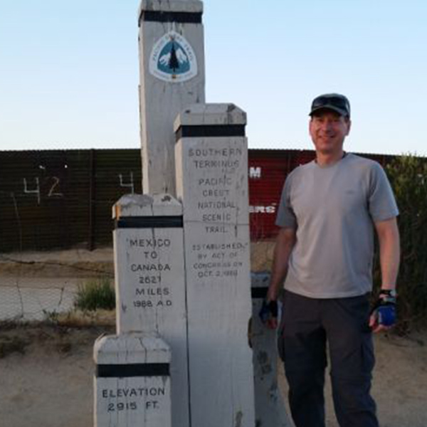 Rich Brinkman stands next to a Pacific Crest Trail marker.