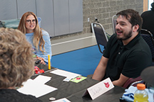 Edwardo Alcantar sits at a table talking with three staff members.