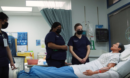 Nursing students stand around medical dummy in bed