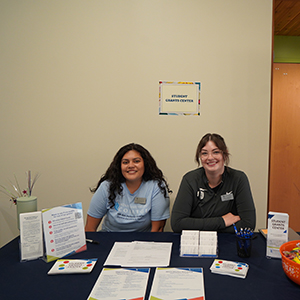 Two Student Grants Center staff members sit at a table with a black and white WVC tablecloth.