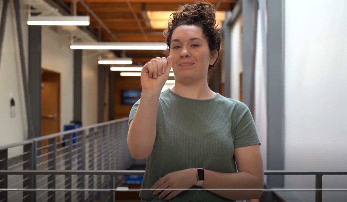 An ASL interpreter holds up her hand in a sign language gesture.