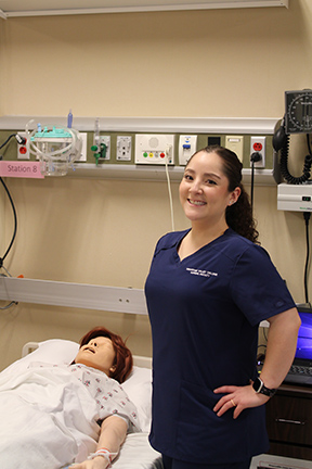 Professor Carolina Martinez Calderon stands next to a manikin in a nursing simulation lab.