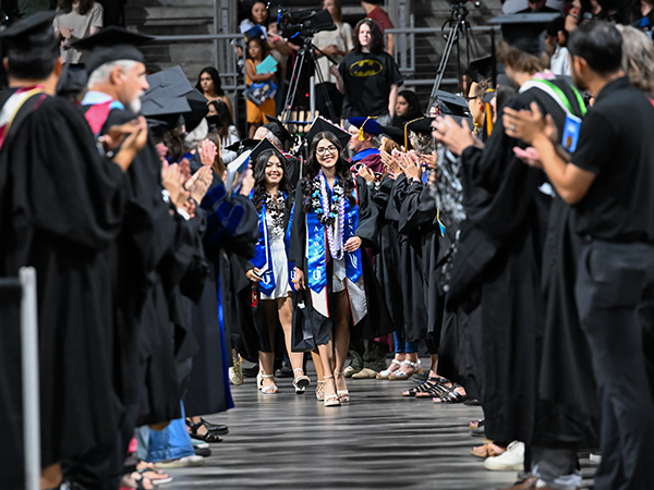 WVC graduates walk between two rows of WVC faculty who are clapping for them at a graduation ceremony.
