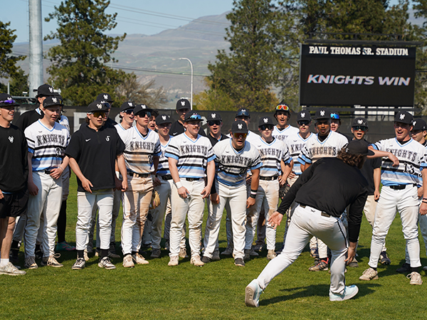 The Knights baseball team stand together with a stadium sign in the background that says "Knights Win."