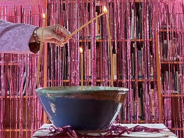 A blue and green ceramics bowl holds three unlit candles, and a hand holds a lit candle against the wick of an unlit candle.