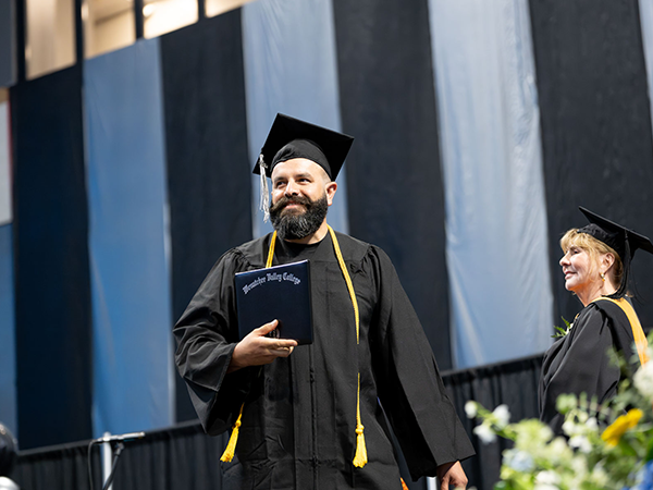 A graduate walks across stage holding his diploma.
